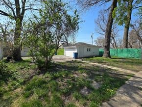 Gary house for rent - A small white house with a blue door is surrounded by trees and grass.