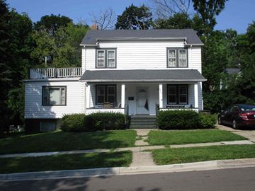 East Lansing apartment for rent - A white two-story house with a porch and a car parked in front.