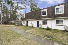 Columbia apartment for rent - A white house with a black door and windows is surrounded by a grassy area and trees.