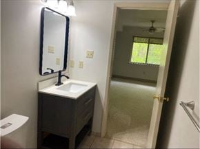 Kitchener house for rent - A bathroom with a sink, mirror, toilet and a door leading to a hallway.