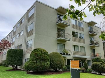 Victoria apartment for rent - Apartment building with green bushes in front.