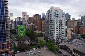 Calgary apartment for rent - A cityscape with a large building in the foreground and a green mural on the side of a building.