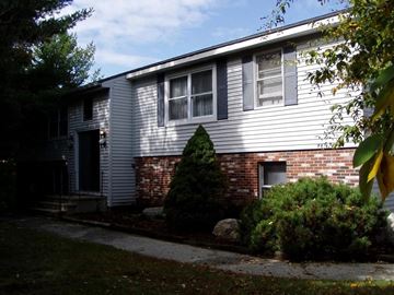 Derry apartment for rent - A house with a grey siding and a brick chimney.