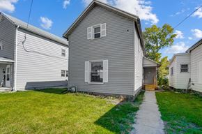 Lima house for rent - A house with a grey siding and a brown door is surrounded by a grassy lawn.