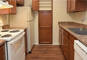 Baton Rouge apartment for rent - A kitchen with a white stove top oven, white dishwasher, and brown cabinets.