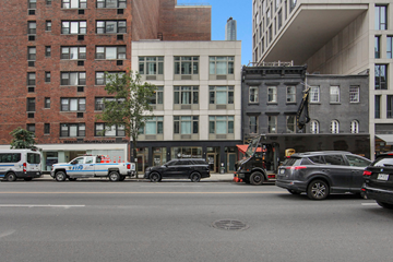 New York apartment for rent - A black car is parked in front of a building with a white truck and a blue van behind it.