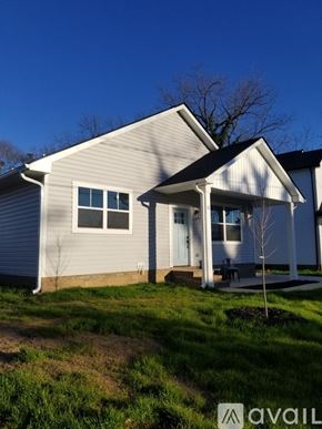 Greenville house for rent - A house with a white door and windows is surrounded by grass and trees.