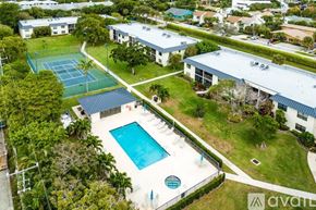 Delray Beach condo for rent - A tennis court is surrounded by a pool and a tennis court building.