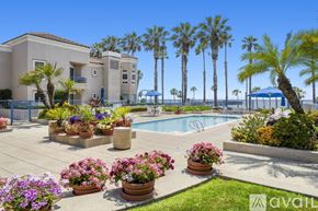Oceanside apartment for rent - A pool surrounded by chairs and umbrellas with a building in the background.