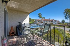 Carlsbad apartment for rent - A patio with chairs and a table is overlooking a pool and a building.