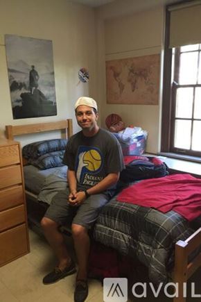 Marrero house for rent - A man in a black shirt and plaid shorts sits on a bed in a room with a world map on the wall.