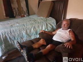 Marrero house for rent - A man in a white tank top and black shorts is sitting on a brown couch.