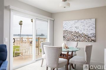Oceanside apartment for rent - A living room with a glass table and chairs, a painting, and a view of a balcony with a palm tree.