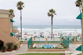 Oceanside apartment for rent - A beach scene with people on the sand and palm trees.