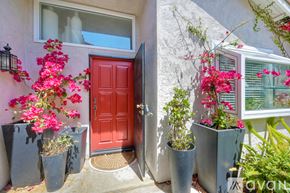 Oceanside apartment for rent - A red door is flanked by two grey planters with pink flowers.