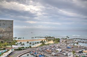 Honolulu apartment for rent - A view of a beach with a parking lot and a tall building in the background.
