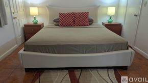 Miami apartment for rent - A bed with a grey sheet and two red pillows with a lamp on each side.