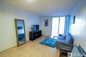 Miami condo for rent - A living room with a grey couch, a blue rug, and a wooden floor.