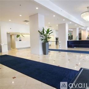 Miami Beach condo for rent - A spacious lobby with a blue carpet and a large plant in a black pot.