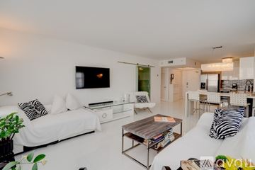 Miami Beach condo for rent - A living room with a white couch and a television on the wall.