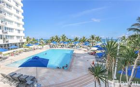 Miami Beach condo for rent - A large swimming pool surrounded by palm trees and lounge chairs.