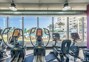 Miami Beach condo for rent - A gym with treadmills and a view of the pool and buildings outside.
