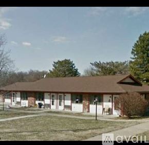 Delphos apartment for rent - A house with a brown roof and white walls is surrounded by a grassy area and trees.