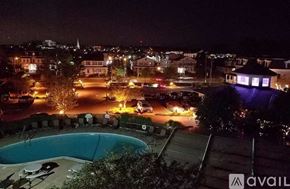 Norwalk apartment for rent - A pool surrounded by trees with a cityscape at night.