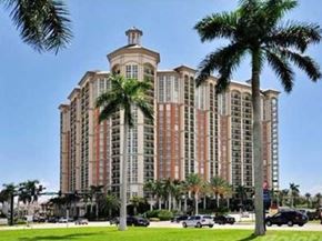 West Palm Beach apartment for rent - A large, multi-story building with a red and beige facade is surrounded by palm trees.