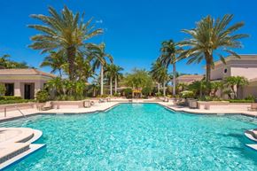 Palm Beach Gardens condo for rent - A large swimming pool surrounded by palm trees and a clear blue sky.