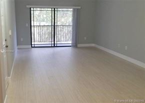 Palm Beach Gardens condo for rent - A spacious room with light wood flooring and a sliding glass door leading to a balcony.