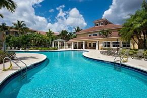 West Palm Beach condo for rent - A large swimming pool in front of a building with palm trees around.