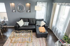 North Hollywood townhouse for rent - A black couch with a yellow throw pillow sits in front of a grey wall with a mirror and two wall sconces.