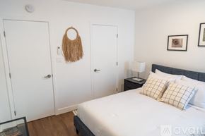 North Hollywood apartment for rent - A bedroom with a bed, two pillows, a woven bag on the wall, and a lamp on a nightstand.