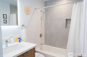 Los Angeles house for rent - A bathroom with a white sink, a shower with a white curtain, and a clock on the wall.