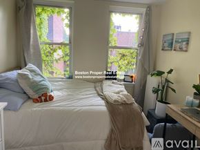 Boston apartment for rent - A bedroom with a bed, a window with curtains, a nightstand with a lamp, a plant, and a picture on the wall.