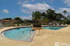 West Palm Beach condo for rent - A large outdoor swimming pool surrounded by palm trees and lounge chairs.