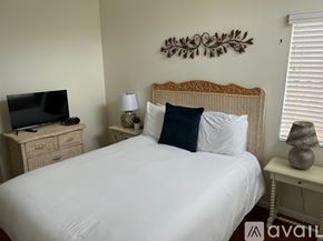 Oceanside apartment for rent - A bedroom with a white bed, a television on a cabinet, and a wall decoration.