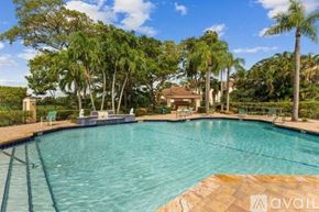 West Palm Beach condo for rent - A swimming pool surrounded by palm trees and a house in the background.