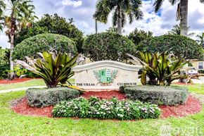 West Palm Beach condo for rent - The Villas Clubhouse sign is surrounded by greenery and flowers.