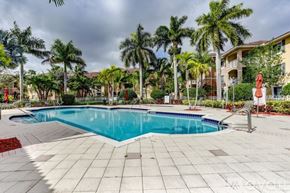 West Palm Beach condo for rent - A swimming pool surrounded by palm trees and a red sculpture.