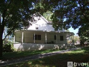 Ellicott City house for rent - A house with a white fence and a porch is surrounded by trees.