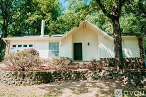 Little Rock house for rent - A white house with a green door and windows is surrounded by trees.