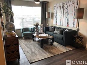 Little Elm apartment for rent - A living room with a black couch, a blue chair, a wooden coffee table, and a large window with blinds.