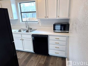 Warr Acres house for rent - A black refrigerator stands next to a white sink in a kitchen.