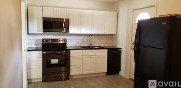 Natchitoches apartment for rent - A black refrigerator stands in a kitchen with white cabinets and a black countertop.