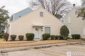 Shreveport townhouse for rent - A house with a white door and windows is surrounded by bushes.