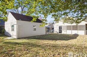 Tulsa house for rent - A small white house with a brown roof is surrounded by trees with yellow leaves.