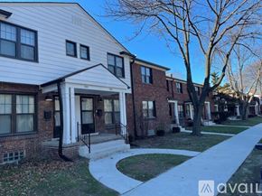 Detroit apartment for rent - A white house with a black door and windows is in front of a tree and other houses.