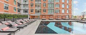 North Bergen condo for rent - A large pool surrounded by lounge chairs in front of a red brick building.